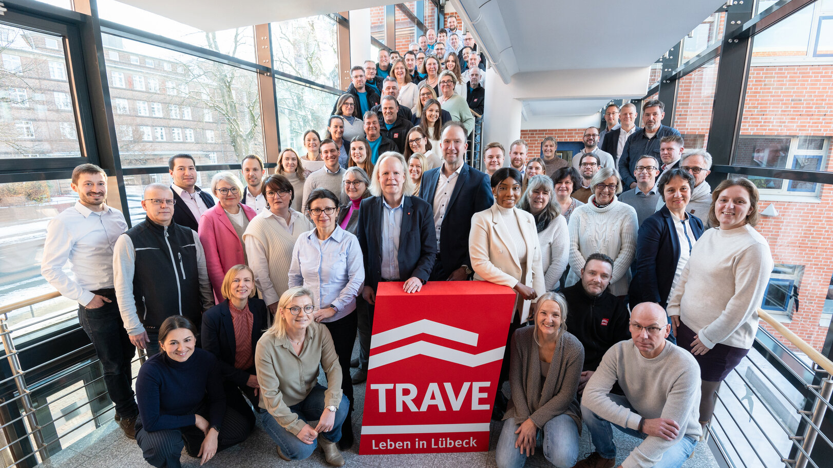 Das TRAVE-Team im Treppenhaus der Falkenstraße 11. Im Vordergrund das TRAVE-Logo und die Geschäftsführer Dr. Matthias Rasch und Sebastian Weist.