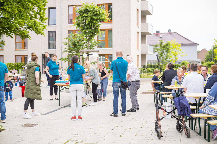 Mitarbeiterinnen und Mitarbeiter der TRAVE bei einem Mieterfest. In einem schönen Innenhof der Artlenburger Straße sitzen die Menschen an Tischen und stehen in Gruppen zusammen und reden miteinander.