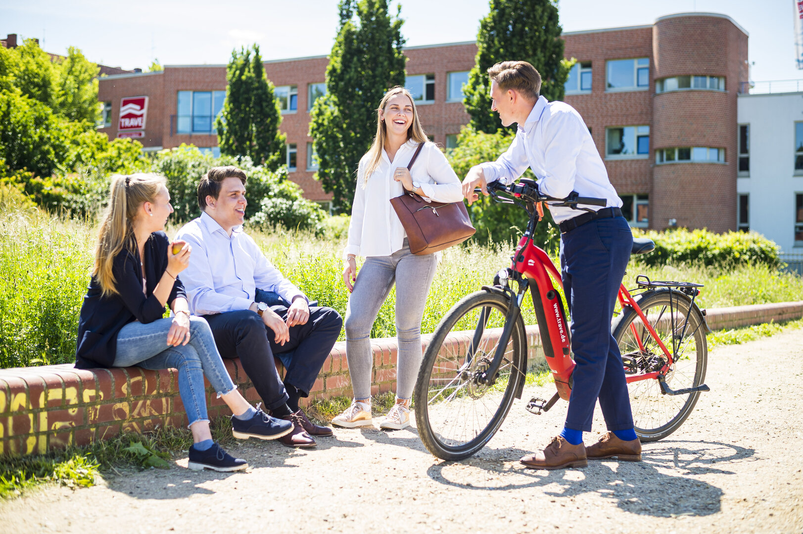 Die TRAVE bildet Immobilienkaufleute aus Eine Gruppe von vier Auszubildenden unterhält sich entspannt. Im Hintergrund das Firmengebäude der TRAVE.